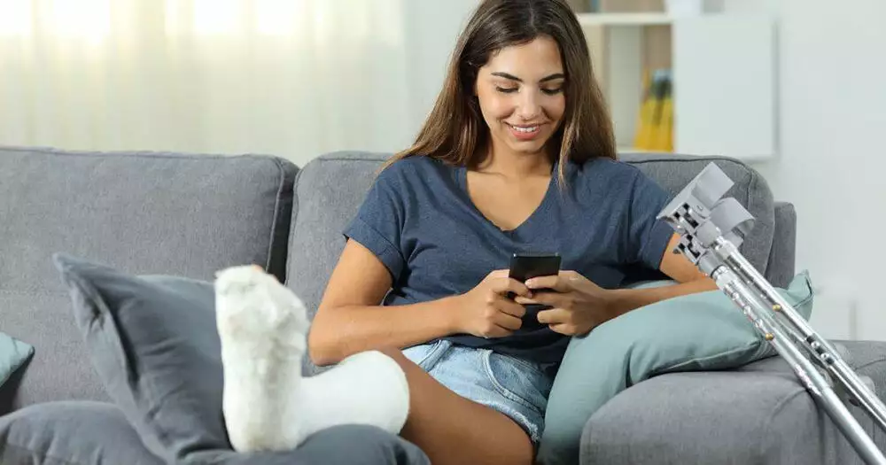 A woman with a prosthetic leg, happily texting while sitting on a gray sofa