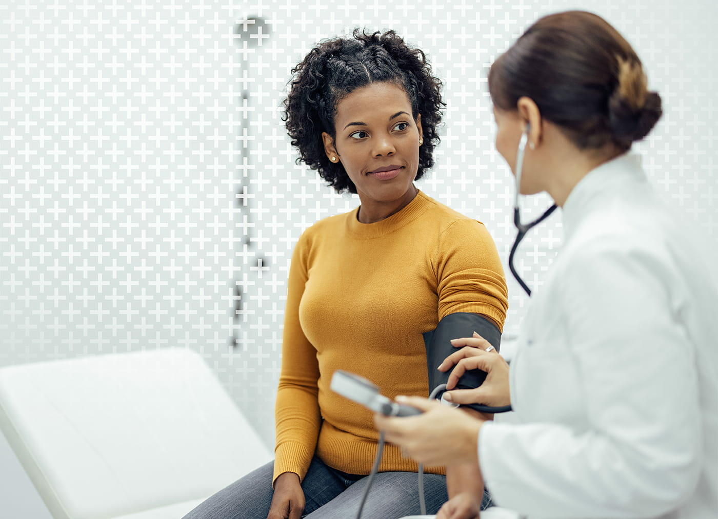A woman sitting on a bed with a stethoscope around her arm, indoors.