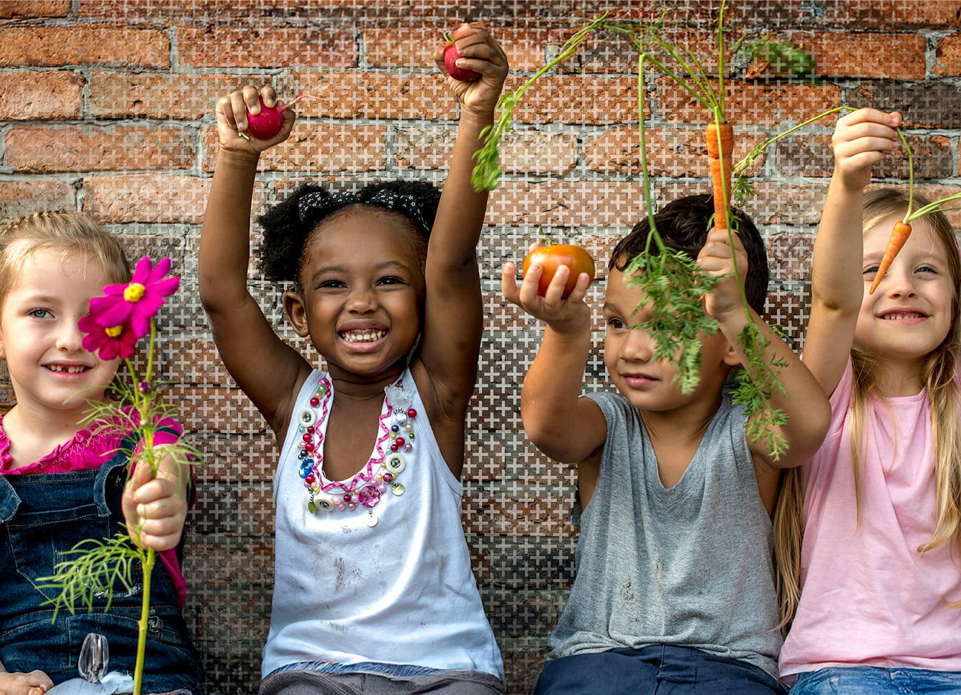 A group of children outdoors, smiling and holding a variety of vegetables.