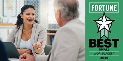 Smiling woman in a blazer speaks with an older man across a laptop, beside a green Fortune Best Small Workplaces 2026 award graphic.